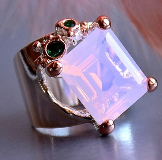 The Pink Dusk Zircon Ring has tiny green zircons. Made of copper, rose gold plated. Abstract, modern design. Has a shine finish. Rectangle cut in a prong setting. 