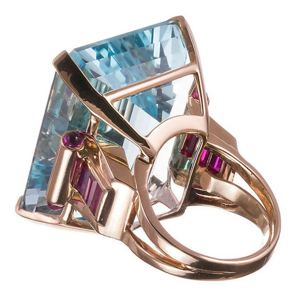 This Aquamarine Cubic Cocktail Ring is a large dreamy rectangle ring. It is crafted with a rich aquamarine and rose gold tone hue. A statuesque blue crystal like stone in the centre.