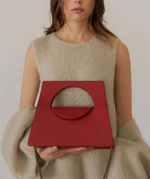 The Apollo Geometric Handbag is a trapezoid shape clutch with a half circle cut out, and easy to open button clasp. Transforms into a cross body with removable, long chain strap.