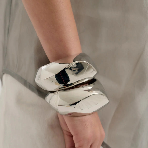 This large bangle bracelet features a striking geometric design in silver and gold tones, offering a modern and versatile accessory for any outfit. 