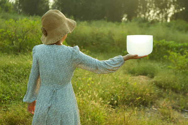 Person holding a white singing bowl in a natural setting